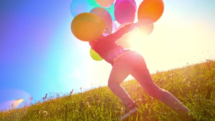 SLO MO小女孩拿着一堆彩色气球在阳光明媚的草地上奔跑