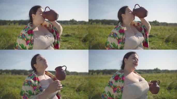 可爱的超重女人喜欢在绿色的夏日田野上喝从土壶里喝新鲜的牛奶。