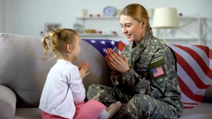 快乐的美国女兵和孩子在沙发上玩手，孩子拥抱着妈妈