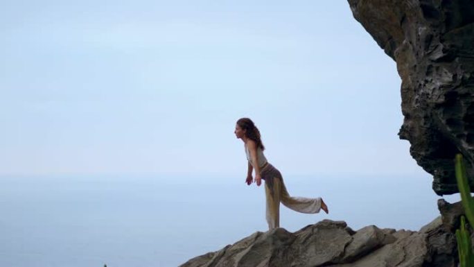 日落时在岩石海岸上做瑜伽的年轻女子。健康生活方式的概念。和谐。人与自然。蓝色海洋的背景。
