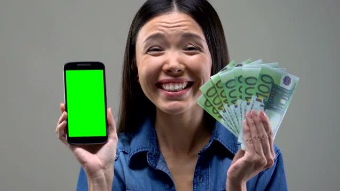 兴奋的亚洲女性展示智能手机和一堆欧元，现金返还服务