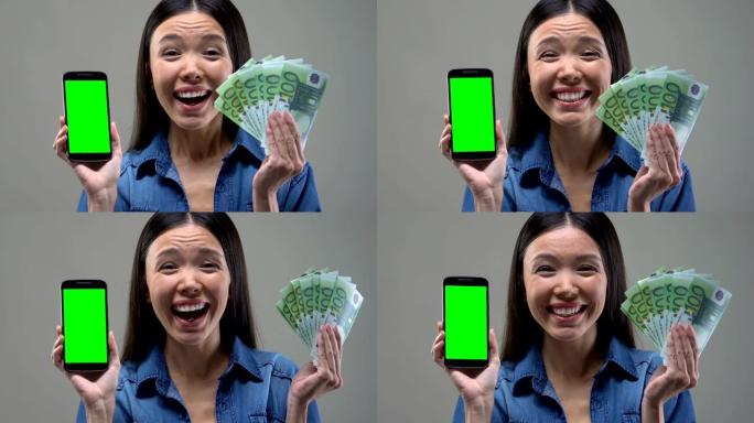 兴奋的亚洲女性展示智能手机和一堆欧元，现金返还服务