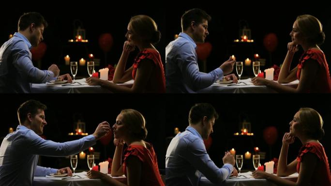英俊的男人喂养漂亮的女士，夫妇在餐厅吃浪漫的晚餐