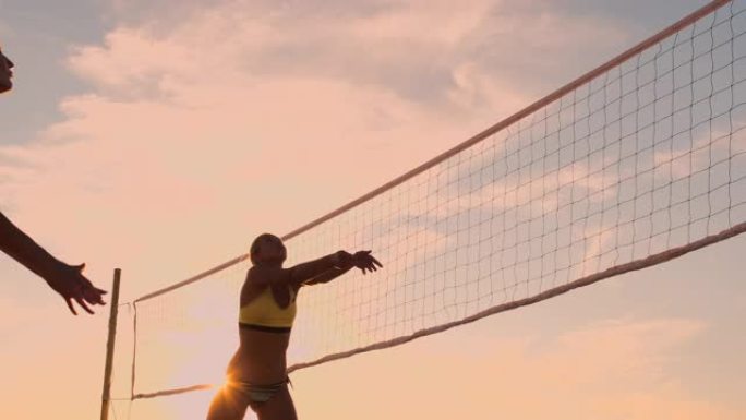 在一个美丽的夏日夜晚，打沙滩排球的运动女孩在空中跳跃并将球击过网。高加索女人得分