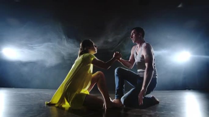 一个男人和一个女人一起跳舞，穿着牛仔裤跳舞，穿着黄色衣服在舞台上抽烟。音乐剧