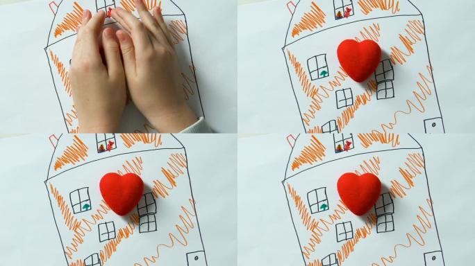 Childs双手将玩具心放在房子的图画上，孤儿梦dream以求的家