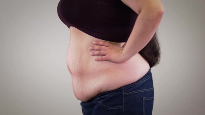 肥胖的无法识别的白人妇女的特写镜头缩回腹部并放松。肥胖女性身体的侧视图。肥胖，超重问题。