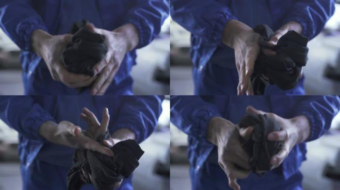 一位身穿制服的未被识别的汽车修理工站在服务站修理汽车后，用抹布擦拭弄脏的手。