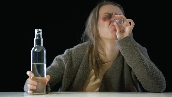 无望的嗜酒成瘾的女人脸上有伤口往杯子里倒伏特加