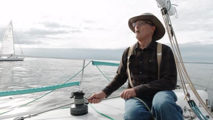 一名60多岁的男子在华盛顿的普吉特海湾 (Puget Sound) 的帆船上的绞盘上拉紧绳子，而他的