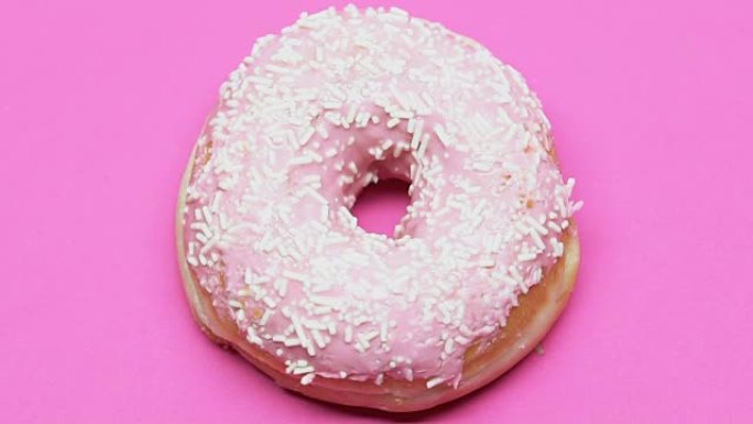 在粉红色的桌子上旋转甜甜圈，高糖甜点引起糖尿病，诱惑