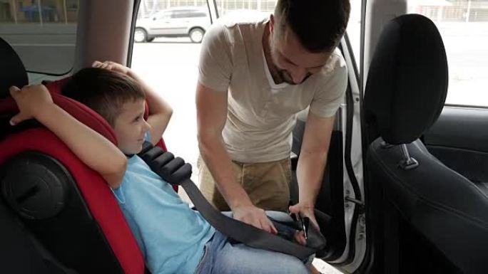 婴儿汽车座椅上的微笑儿子被有爱心的父亲放在车后