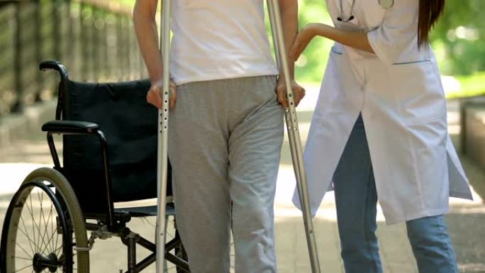 物理治疗师帮助坐在轮椅上的病人拄着拐杖走路