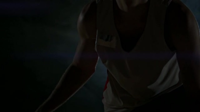 运球篮球运动员在黑暗的房间里的特写镜头在慢动作中