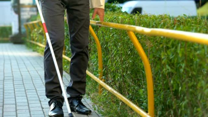 一名视力受损的男子用白色藤条在室外的走道上寻找栅栏