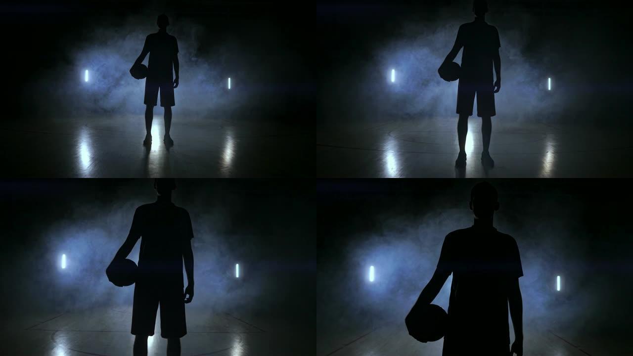 篮球场上黑黑的背景上有烟的篮球运动员的剪影投掷篮筐球，以慢动作看着镜头