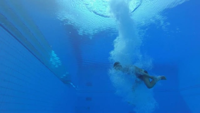 SLO MO LD男潜水员降落在游泳池中，并在水下向水面游泳