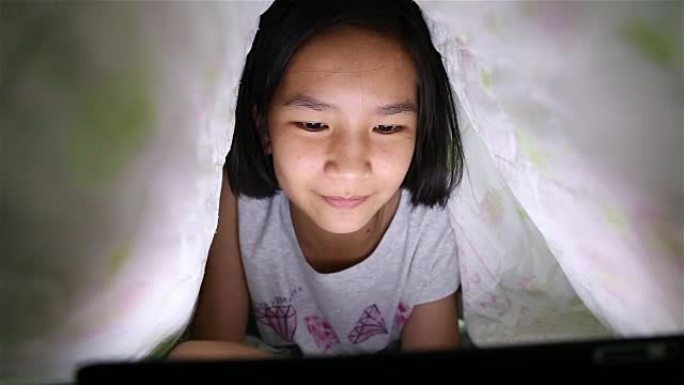 亚洲女孩在床上玩平板电脑。