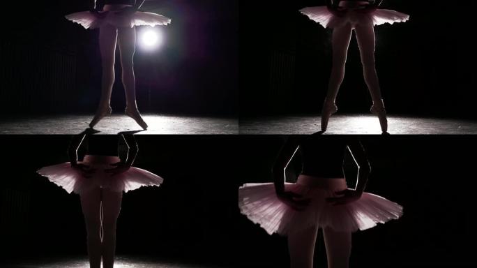 芭蕾舞者在黑暗工作室练习练习。演播室黑色背景上聚光灯下芭蕾舞女演员的剪影。芭蕾舞女演员穿着芭蕾舞短裙