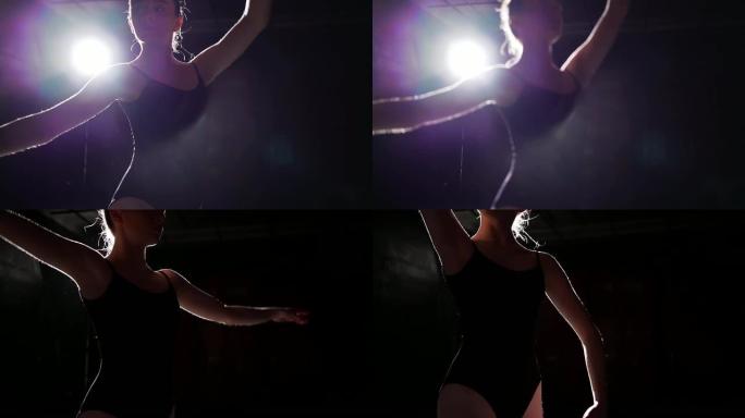 肖像专业芭蕾舞演员站在工作室黑色背景上的聚光灯下。芭蕾舞演员展示经典芭蕾舞剧。慢动作。
