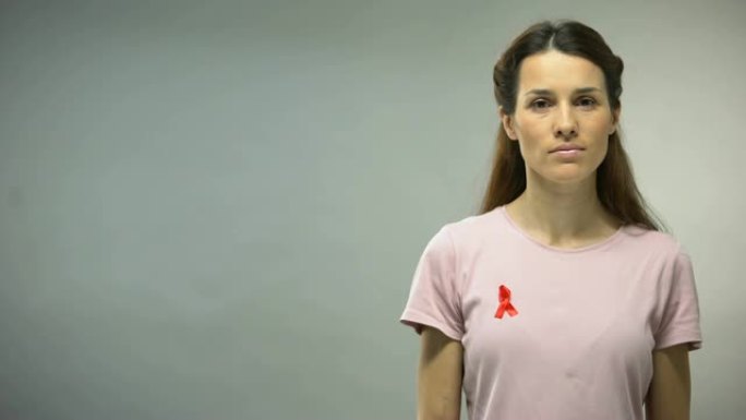一名身穿红丝带衬衫的年轻女子在镜头前看着，这是艾滋病防治意识的标志