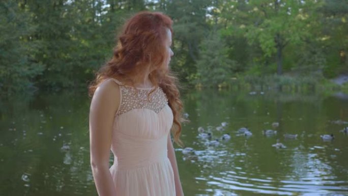 迷人的年轻白人妇女的侧视图，穿着白色长裙，红头发，站在河岸上，微笑着