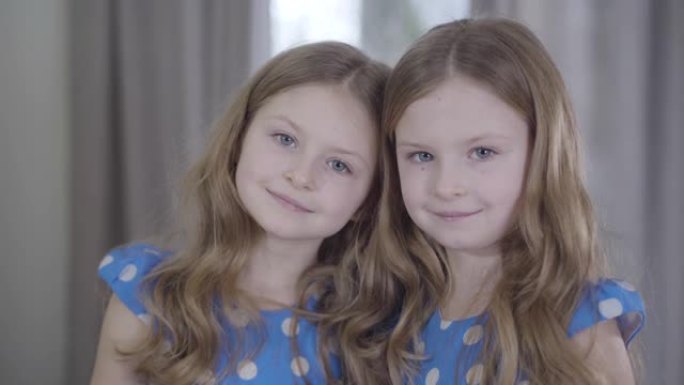 相机远离迷人的双胞胎小姐妹在镜头前微笑的面孔。快乐友好女孩在家摆姿势的肖像。团结、休闲、生活方式、家