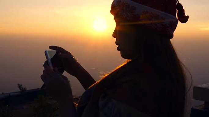 用智能手机拍摄日出美景的女人的剪影
