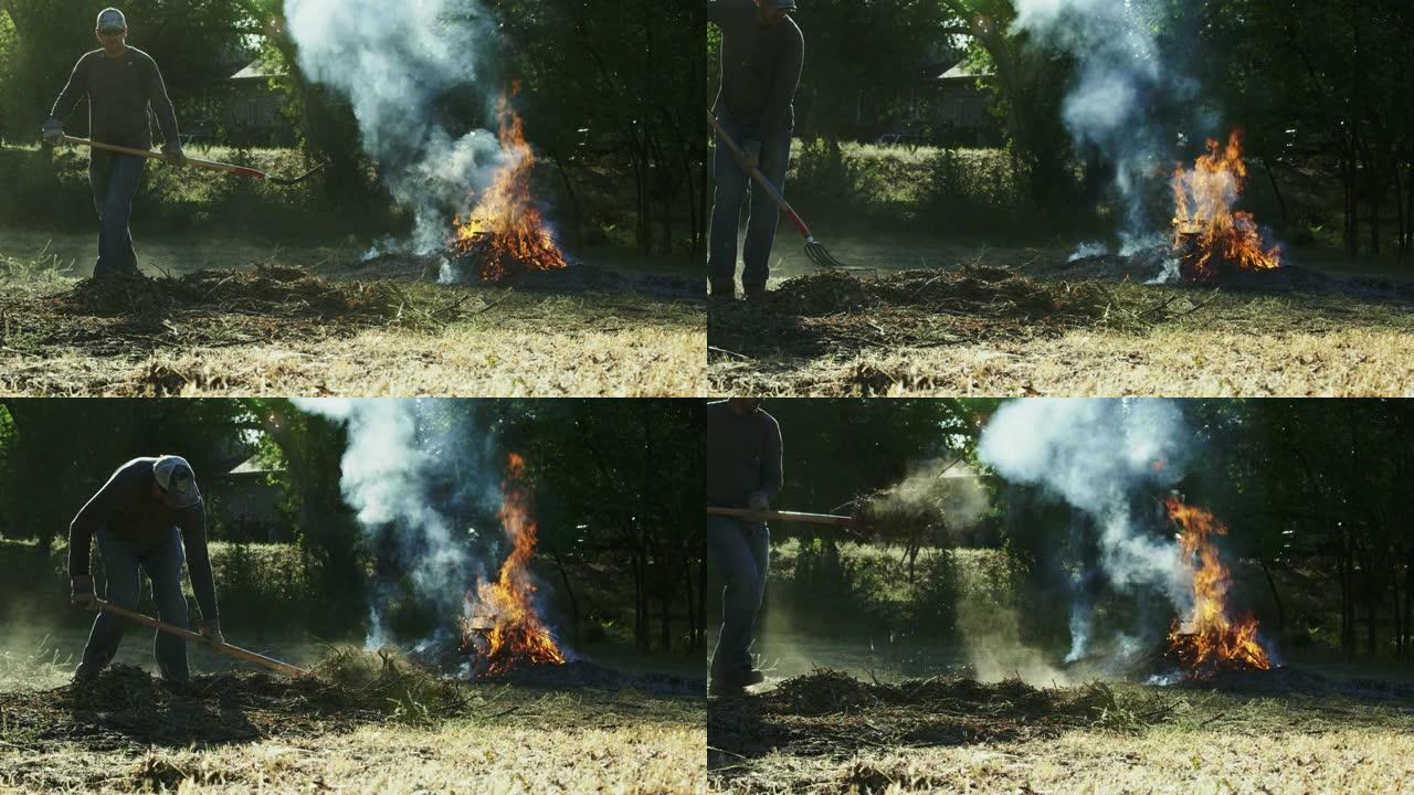 一个四十多岁的高加索人用干草叉拿起木棍和树枝，走向户外的一个大火烧堆