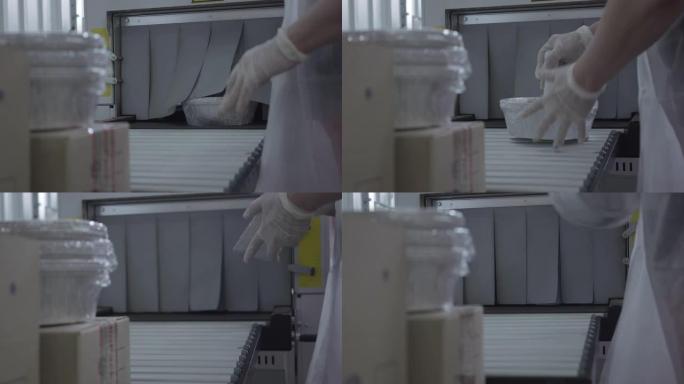 女性高加索人的手从吸尘机中取出包装好的碗碟容器。无法辨认的女人在生产线上使用设备。商业、输送机、工业
