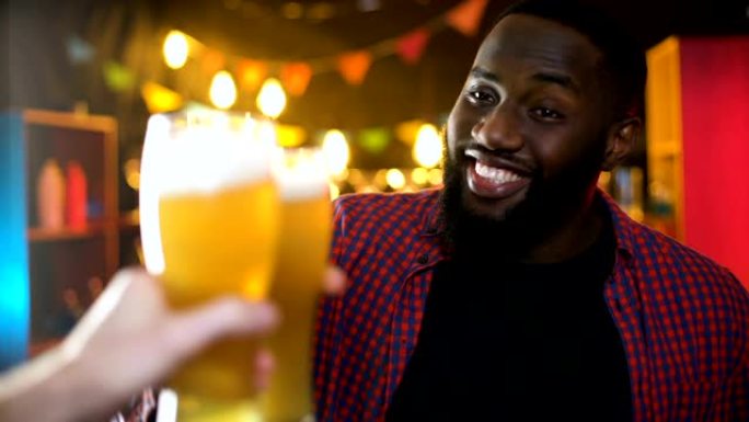 开朗的非洲裔美国男性碰杯啤酒杯，在酒吧享受成绩