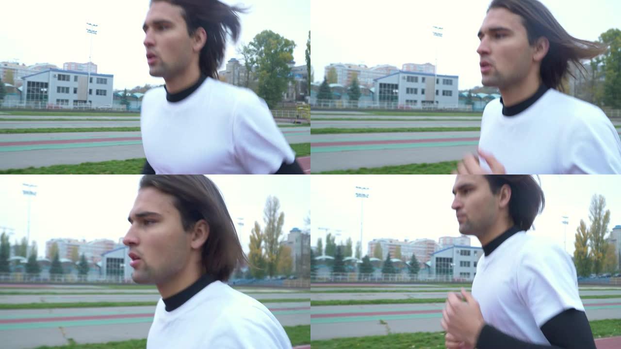 穿着运动t恤的年轻人在体育场跑步。黑头发的帅哥在户外慢跑。在操场上跑步的体育人。健康的生活方式