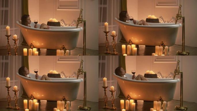 女人躺在泡泡浴中，用蜡烛发出的光放松和喝葡萄酒。浪漫放松的芳香疗法氛围。带蜡烛的浴室