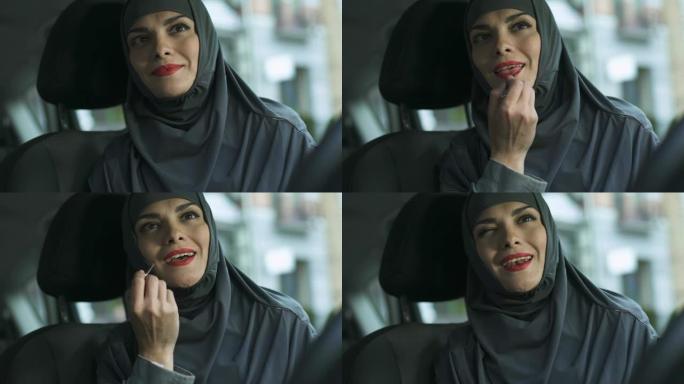 自信的阿拉伯女士在自动应用红色口红，调情眨眼