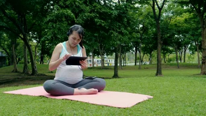 年轻孕妇在户外健身并使用平板电脑
