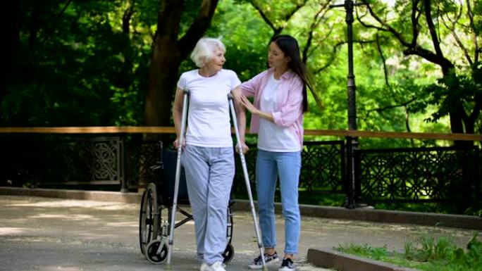 年轻女子帮助老太太拄着拐杖行走，髋部骨折康复