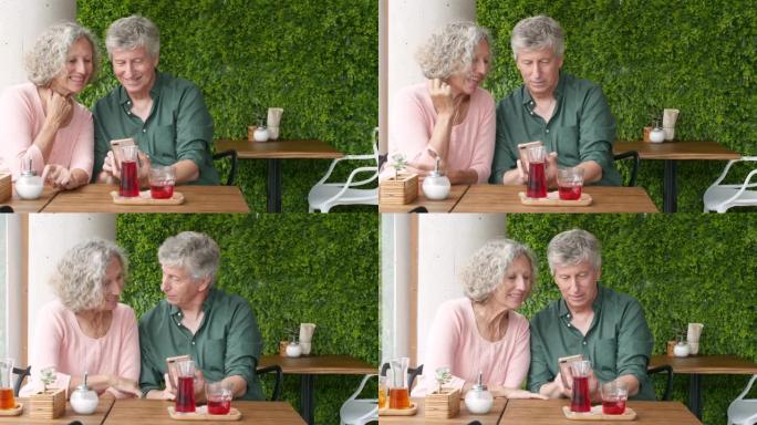快乐的高级男子坐在餐厅时在智能手机上展示女性照片