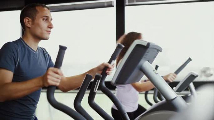 有氧运动机器上的男人和女人: 在健身房进行艰苦的训练