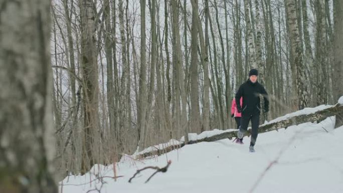 在阳光明媚的冬日早晨，积极美丽的年轻健康夫妇穿着运动服穿过森林。跳过树，克服路径的困难。越过障碍物