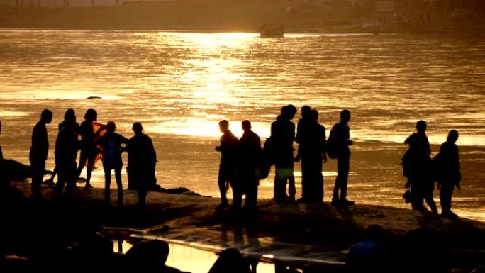许多年轻人站在神圣的恒河岸边的石头上，在来自水面的日落反射黄光中，印度瑞诗凯诗，做了一个一般的自拍