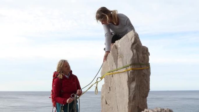 两个女人爬上海面上的垂直岩石，日出