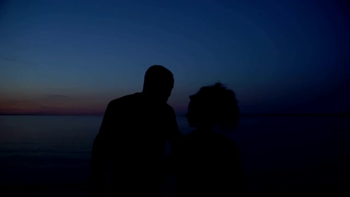 幸福的夫妇在夜海背景下拥抱的剪影，团结
