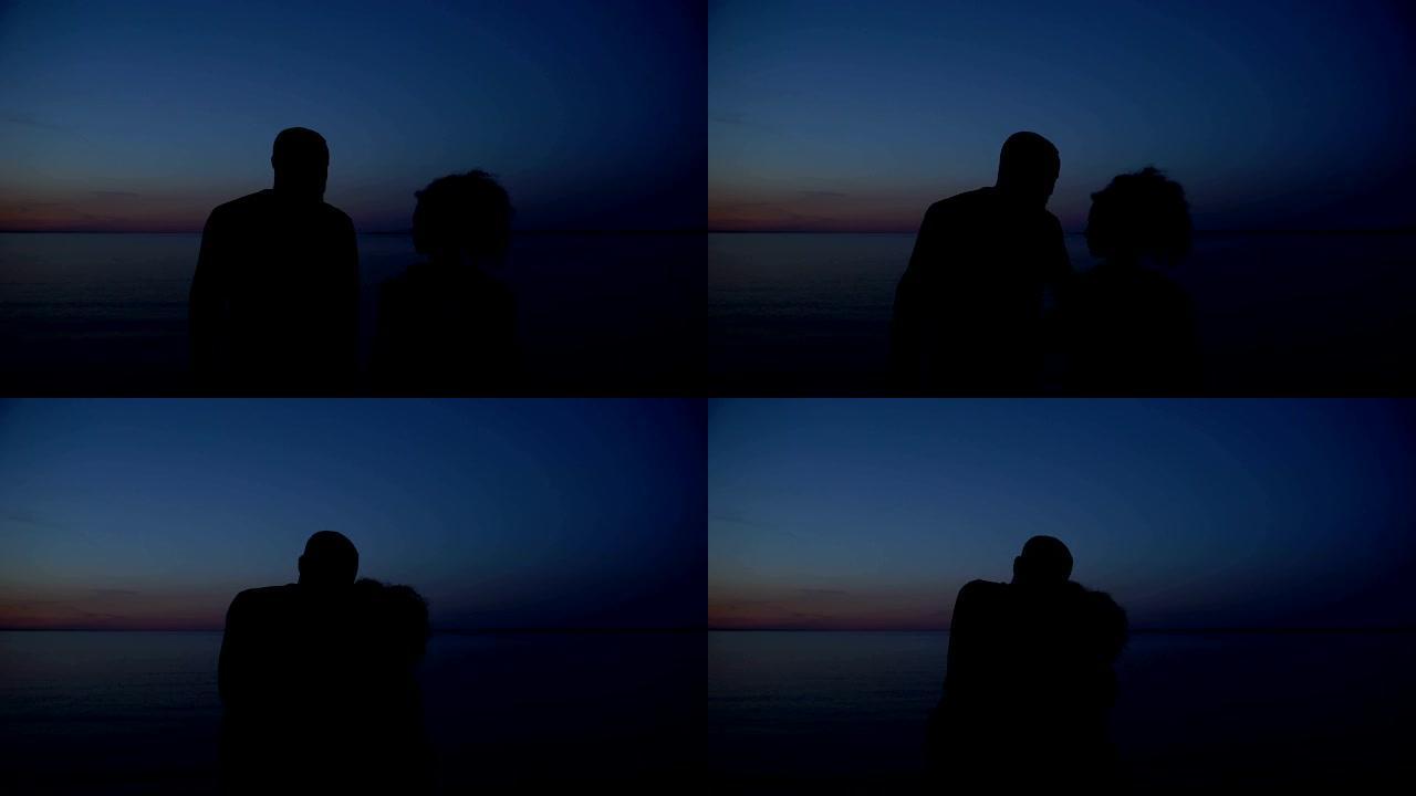 幸福的夫妇在夜海背景下拥抱的剪影，团结