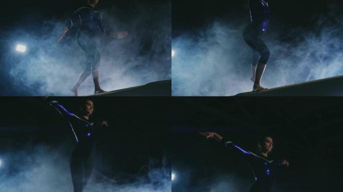 女孩体操运动员的腿的特写镜头在烟雾和慢动作中进行平衡木跳跃