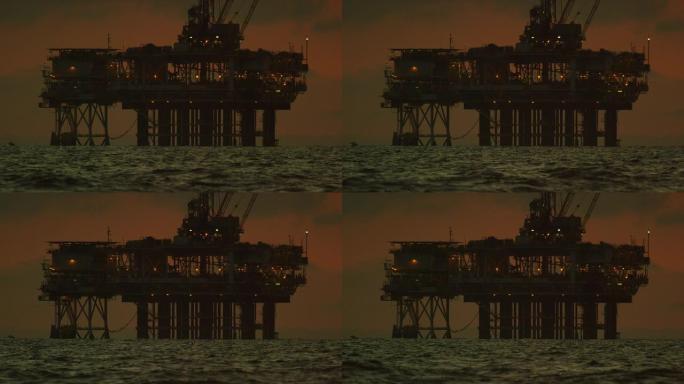 地平线上的海上石油钻机平台的慢动作拍摄，日落时分，在戏剧性的暴风雨天空下，海浪在前景中