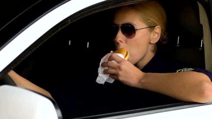 女警察在巡逻车里吃汉堡，不健康的零食，消化问题的风险