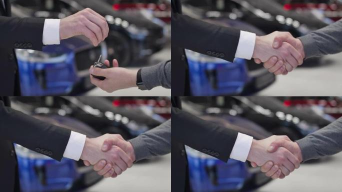 男性高加索人的特写镜头给顾客提供车钥匙并握手。经销商和客户就汽车购买达成协议。汽车经销商，汽车工业。