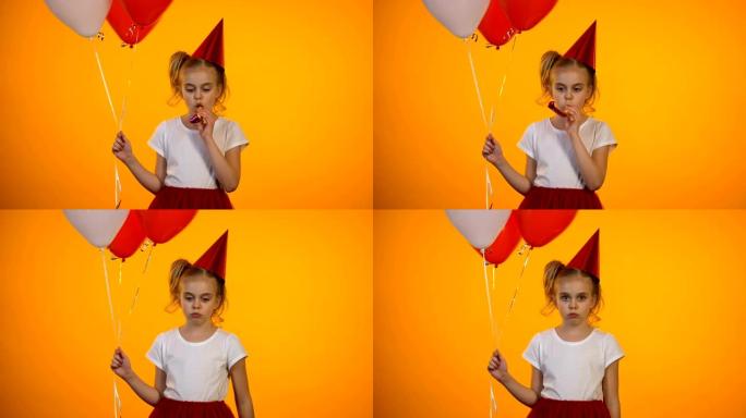 沮丧的女孩吹着派对号角，拿着气球，独自庆祝生日