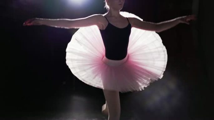 在工作室的黑色背景上，优雅灵活的女孩在她的尖头芭蕾舞鞋上跳舞。专业芭蕾舞演员穿着芭蕾舞短裙和脚尖鞋展
