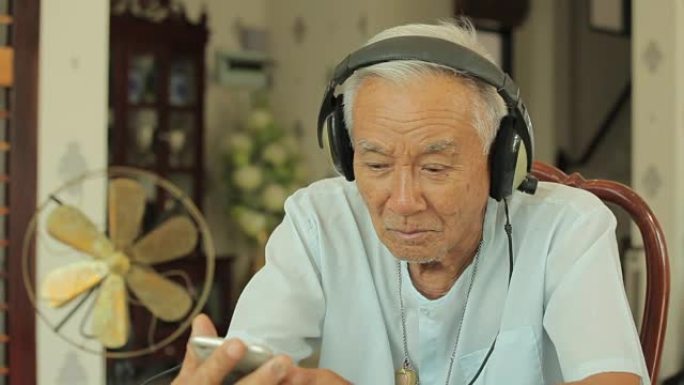 快乐亚洲老人耳机在家听音乐
